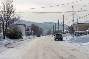 Kanada, 25 Ocak 2026: Kış sokağı manzarası, karla kaplı yol, park edilmiş arabalar, elektrik hatları, konut evleri
