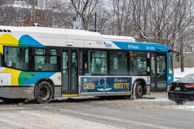 Kanada, Montreal, 25 Aralık 2025: Şehir otobüsü kış reklamlarıyla karlı sokaklarda geziniyor.