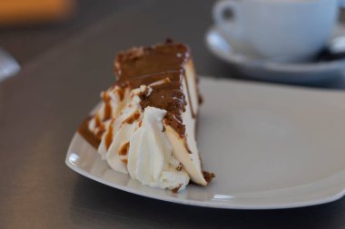 Kremalı bir parça cheesecake, ve üstüne çikolata, beyaz bir tabakta servis edilir.