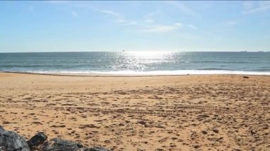 İspanya, Endülüs 'teki Mazagon Sahili' nde, parlak güneşli bir gökyüzü altında uzak kargo gemileriyle altın kumun geniş açılı görüntüsü ve sakin mavi deniz..