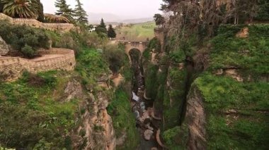 Tarihi Puente Viejo Köprüsü 'nün geniş açılı sineması. Dik Tajo de Ronda Kanyonu' nu, Endülüs, Malaga, İspanya 'da yemyeşil ve yemyeşil bir nehir ile geçiyor..