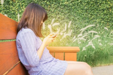 Gülümseyen güzel mutlu karışık yarış Asyalı kız genç kadın genç kadın, Sonbahar ya da sonbaharda bir bankta oturan cep telefonu mesaj.