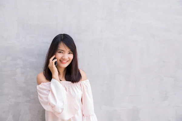Kaunis aasialainen nuori nainen puhuu matkapuhelimella, betoniseinän yli — kuvapankkivalokuva