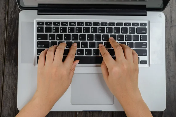 Mandlige hænder, der arbejder på en hvid bærbar computer på et træskrivebord - Stock-foto