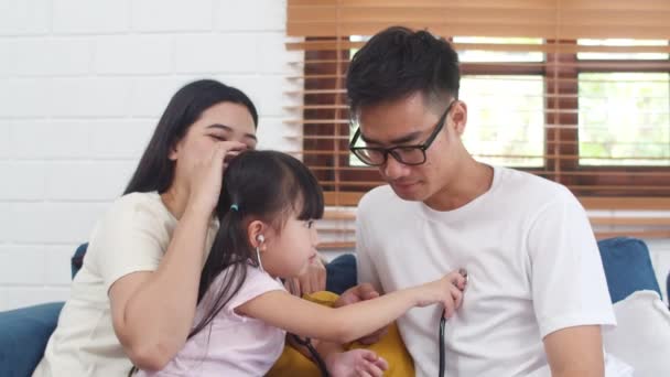 幸せな陽気なアジアの家族のお父さん お母さんと娘は家でソファで楽しんでいる医者として面白いゲームをプレイします 自己分離 自宅に滞在 社会的距離 コロナウイルスの予防のための隔離 — ストック動画