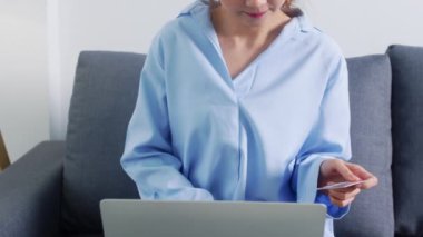 Dizüstü bilgisayar, kredi kartı ve e-ticaret interneti kullanan genç bir Asyalı kadın. Evdeki oturma odasında. Evde kal, online alışveriş, kişisel izolasyon, sosyal uzaklık, koronavirüs için karantina.