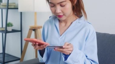Genç Asyalı bayan evdeki oturma odasında akıllı telefon, kredi kartı satın alma ve e-ticaret interneti kullanıyor. Evde kal, online alışveriş, kişisel izolasyon, sosyal uzaklık, koronavirüs için karantina.