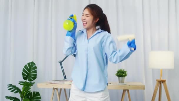 有趣而快乐的年轻亚洲女人拿着喷雾机 一边在现代客厅里唱歌 一边在屋里料理家务 家庭妇女的生活方式概念 慢动作射击 — 图库视频影像