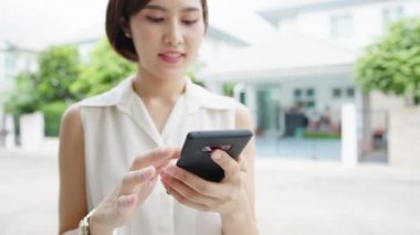 Çekici genç Asyalı iş kadını cep telefonu kullanıyor sosyal medya internetini kontrol ediyor, sokakta arkadaşlarıyla sohbet ediyor. Coronavirüs ve sosyal uzaklıktan sonra yeni bir yaşam tarzı..