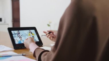 Dijital tablet kullanan Asyalı müslüman kadın, evdeki oturma odasında uzaktan çalışırken online beyin fırtınası denilen toplantı planından meslektaşına bahsediyor. Corona virüsü için sosyal uzaklık, karantina.