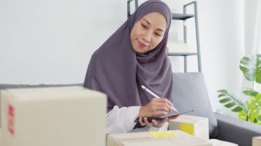 Genç Asyalı Müslüman iş kadını hisse senedi alım siparişini kontrol ediyor ve merkez ofisindeki tablet bilgisayarlara kaydediliyor. Küçük işletme sahibi, çevrimiçi pazar teslimatı, yaşam tarzı serbest konsepti.