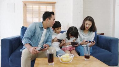 Mutlu Asyalı aile babaları, anne ve çocuklar akıllı telefondan komik oyunlar oynuyorlar evdeki oturma odasında koltukta oturuyorlar. Kendini soyutlama, evde kalma, sosyal mesafeler, koronavirüs önleme için karantina.