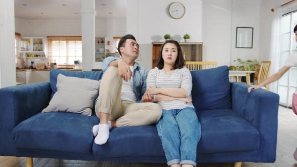 アジアの家族のお父さんとお母さんはソファに座って 娘と息子は自宅のリビングルームでソファの周りを実行する楽しい叫びを持っている間に疲れを感じています 社会的距離 コロナウイルス防止のための隔離 — ストック動画
