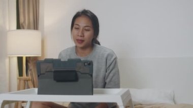 Tablet kullanan Asyalı iş kadını, yatak odasında evde çalışırken iş arkadaşlarıyla görüntülü görüşme planı hakkında konuşuyor. Kişisel izolasyon, sosyal uzaklık, korona virüsünün önlenmesi için karantina.