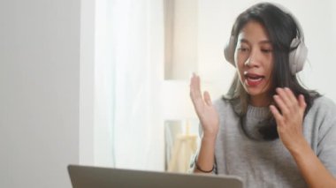 Asyalı iş kadını bilgisayarla iş arkadaşlarıyla video görüşmesinde planlar hakkında konuşurken yatak odasında çalışırken kulaklık takıyor. Kişisel izolasyon, sosyal uzaklık, korona virüsü için karantina.