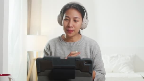 亚洲女商人带着耳机 一边在卧室聪明地从家里工作 一边用平板电脑和同事们谈论视频通话中的计划 自我隔离 社会疏离 电晕病毒检疫 — 图库视频影像