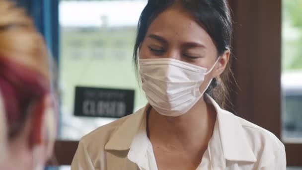 在进入之前 年轻的亚洲女餐馆工作人员戴着防护面罩 在顾客的额头上使用红外温度计检测仪或温度枪 电晕病毒后的新生活方式 — 图库视频影像