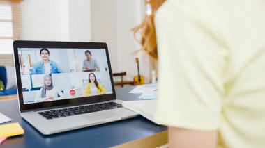 Dizüstü bilgisayar kullanan Asyalı iş kadını, evdeki oturma odasında çalışırken iş arkadaşlarıyla görüntülü görüşme planı hakkında konuşuyor. Kişisel izolasyon, sosyal uzaklık, korona virüsünün önlenmesi için karantina.