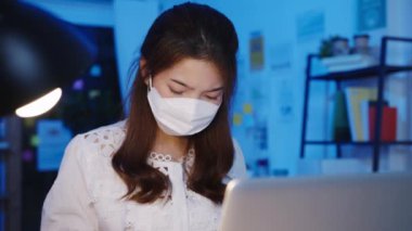 Serbest çalışan Asya 'lı kadınlar yeni ev ofisinde laptoplarını kullanarak yüz maskesi takıyorlar. Geceleri ev aşırı yükleme, kişisel izolasyon, sosyal uzaklık, korona virüsünün önlenmesi için karantina.