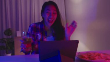 Bira içen genç Asya 'lı bayan eğlenceli anlar yaşıyor disko neon gece partisi etkinliği evdeki oturma odasında video aracılığıyla kutlanıyor. Sosyal uzaklık, koronavirüsün önlenmesi için karantina.