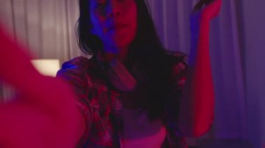 Bira içen genç Asya 'lı bayan eğlenceli anlar yaşıyor disko neon gece partisi etkinliği evdeki oturma odasında video aracılığıyla kutlanıyor. Sosyal uzaklık, koronavirüsün önlenmesi için karantina.