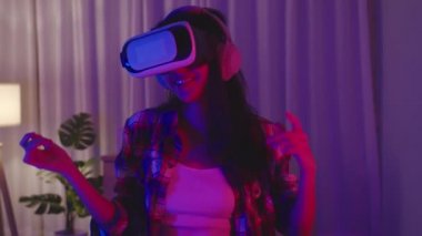 Genç Asyalı bayan, evde oturma odasında neon gece partisi kutlaması yapıp eğlenirken VR kulaklık takıyor ve dans ediyor. Sosyal uzaklık, koronavirüsün önlenmesi için karantina.