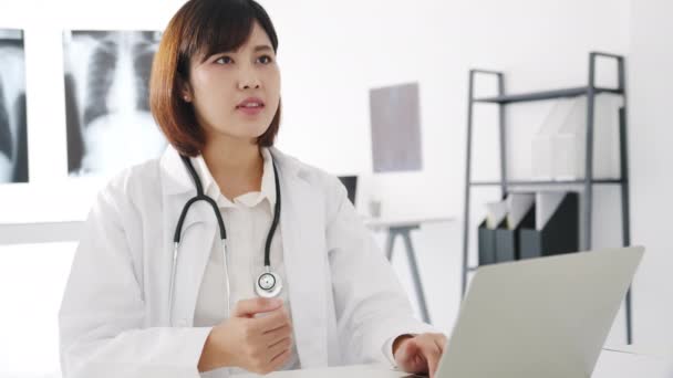 コンピュータのラップトップを使用して白い医療制服を着た若いアジアの女性医師は 健康クリニックや病院のオフィスでデスクに座っている男性患者との素晴らしいニューストークの結果や症状を議論しています — ストック動画