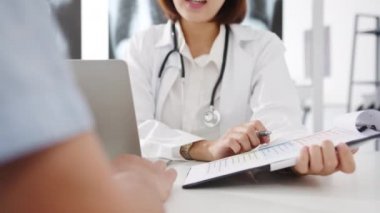 Beyaz üniformalı genç Asya 'lı kadın doktor harika haberler sunuyor. Sonuçları ya da belirtileri sağlık kliniğinde ya da hastane ofisinde masasında oturan erkek hastayla tartışıyor..