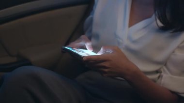 Moda bürosu kıyafetleri içinde başarılı genç Asyalı iş kadını gece geç saatlere kadar şehir modern şehrinde arabanın arka koltuğunda otururken akıllı telefon kullanıyor. İnsanların mesleki tükenme sendromu kavramı.