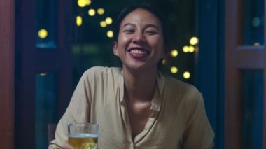 Bira içen genç Asyalı bayan mutlu bir gece partisi yapıyor. Yeni yıl kutlamaları. Gece evde telefonla video aracılığıyla yapılıyor. Sosyal mesafe, koronavirüs karantinası. Bakış açısı veya POV
