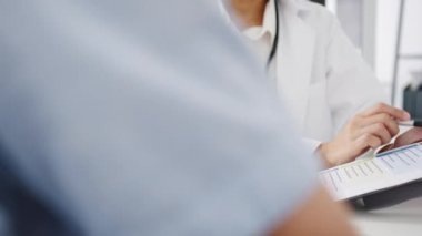 Beyaz üniformalı genç Asya 'lı kadın doktor harika haberler sunuyor. Sonuçları ya da belirtileri sağlık kliniğinde ya da hastane ofisinde masasında oturan erkek hastayla tartışıyor..