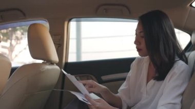 Moda ofis kıyafetleri içinde başarılı genç Asyalı iş kadını sabahın erken saatlerinde şehir merkezinde arabanın arka koltuğunda çalışıyor. İş konseptiyle ilgili işler.