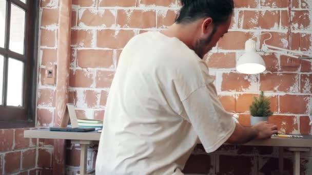 髭を生やしたフリーランスのアジア人男性は 午前中に自宅のリビングルームでノートパソコンで作業を開始します 自宅からの作業 リモートワーク 社会的距離 コロナウイルスの予防のための隔離 — ストック動画