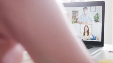 Dizüstü bilgisayar kullanan genç Asyalı iş kadını, evden oturma odasındaki çalışma saatlerinde yapılan telefon görüşmesinin planlarını meslektaşına anlatıyor. Kişisel izolasyon, sosyal uzaklık, korona virüsünün önlenmesi için karantina.