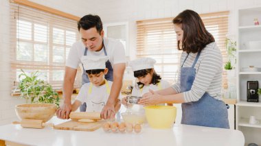 Anaokulu çocuklarıyla birlikte mutlu gülümseyen Asyalı genç Japon ailesi sabahları modern mutfak evinde kahvaltıda pasta ya da pasta pişirirken eğleniyor. Fırın hamuru yoğurur ve kurabiye pişirir..