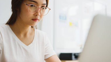 Dizüstü bilgisayar kullanan Asyalı iş kadını, evdeki oturma odasında akıllı bir şekilde çalışırken iş arkadaşlarıyla görüntülü görüşme planı hakkında konuşuyor. Kişisel izolasyon, sosyal uzaklık, korona virüsünün önlenmesi için karantina.