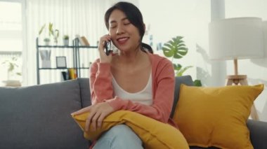 Kanepede oturan güzel Asyalı bayan evdeki arkadaşınla telefon görüşmesi yapıyor. Evde kal, uzun mesafeli ilişki, aile ilişkisi, mesafeyi koru, karantina kavramı.