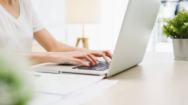 Serbest çalışan Asyalı genç iş kadını evde çalışırken dizüstü bilgisayar kullanıyor. Evden çalışmak, uzaktan çalışmak, kişisel izolasyon, sosyal uzaklık, korona virüsünün önlenmesi için karantina.