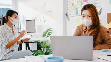 Asyalı iş adamları bilgisayar sunumu toplantısını kullanarak yeni proje arkadaşlarıyla ilgili fikir alışverişinde bulunuyor ve yeni normal ofiste koruyucu yüz maskesi takıyorlar. Coronavirus 'tan sonra yaşam tarzı ve çalışma.