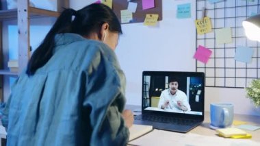 Dizüstü bilgisayar kullanan Asyalı iş kadını iş arkadaşlarıyla oturma odasındaki video görüşme planı hakkında konuşuyor. Geceleri ev aşırı yükleme, uzaktan çalışma, sosyal uzaklık, koronavirüs için karantina.