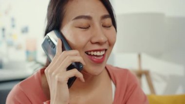 Kanepede oturan güzel Asyalı bayan evdeki arkadaşınla telefon görüşmesi yapıyor. Evde kal, uzun mesafeli ilişki, aile ilişkisi, mesafeyi koru, karantina kavramı.