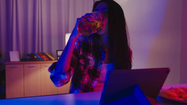 Bira içen genç Asya 'lı bayan eğlenceli anlar yaşıyor disko neon gece partisi etkinliği evdeki oturma odasında video aracılığıyla kutlanıyor. Sosyal uzaklık, koronavirüsün önlenmesi için karantina.