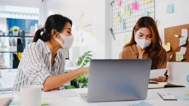 Asyalı iş adamları bilgisayar sunumu toplantısını kullanarak yeni proje arkadaşlarıyla ilgili fikir alışverişinde bulunuyor ve yeni normal ofiste koruyucu yüz maskesi takıyorlar. Coronavirus 'tan sonra yaşam tarzı ve çalışma.