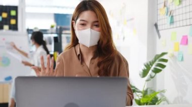 Asyalı iş kadını, iş yerinde çalışırken iş arkadaşlarına bilgisayar sunumu yaparken virüs önleme amaçlı yeni normal bir durumda sosyal mesafeler için yüz maskesi takıyor..