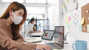 Asyalı iş kadını girişimci yüz maskesi takıyor. Virüs önleme amaçlı yeni normal bir durum için sosyal mesafeye takılıyor. Ofiste dizüstü bilgisayar ve telefon kullanıyor. Corona virüsünden sonra yaşam tarzı.