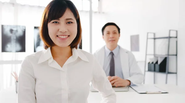 Confident Asia male doctor in white medical uniform and young patient girl looking at camera and smiling while medical consultation at desk in health clinic or hospital. Consulting and therapy concept