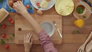 Genç Asyalı kadın şefin elleri seramik kaseye yumurta kırıyor evdeki mutfak masasındaki tahta tahtada sebzelerle omlet pişiriyor. Yaşam tarzı sağlıklı yemek ve geleneksel fırın konsepti. Üst görüntü görüntüsü.