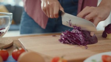 Genç Asyalı kadın şef bıçak tutuyor. Kırmızı Çin lahanasını evdeki mutfak masasında tahta tahtayla kesiyor. Sebze salatası pişirmek, yaşam tarzı sağlıklı yemek yemek ve geleneksel doğal kavram..