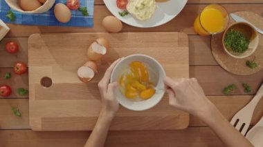 Seramik kâseye yumurta çırpan genç Asyalı kadın şefin elleri mutfak masasındaki ahşap tahtada sebzeli omlet pişiriyor. Yaşam tarzı sağlıklı yemek ve geleneksel fırın. Üst görüntü görüntüsü.