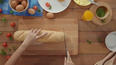 Genç Asyalı kadın şefin elleri bıçakla mutfak masasındaki tahtadan tahıllı ekmeği keser. Taze ev yapımı ekmek üretimi, sağlıklı yemek ve geleneksel fırın konsepti. Üst görüntü görüntüsü.